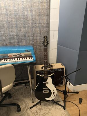 Item 9: black Danelectro double-cutaway electric guitar with a white pickguard, on a stand